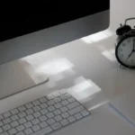 Meja kerja dengan komputer dan jam analog yang menunjukkan waktu kerja kantor